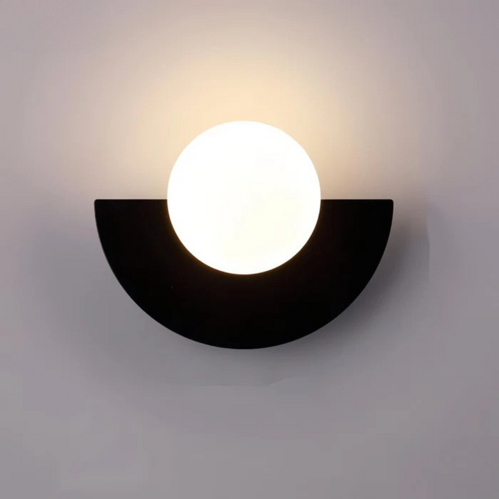 Minimalist clear glass globe LED wall sconce on a black metal arm, mounted on a feature wall