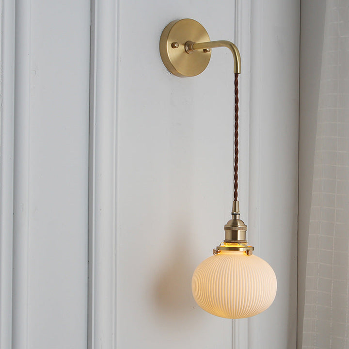Pleated glass shade detail on a brass wall light, diffusing warm light