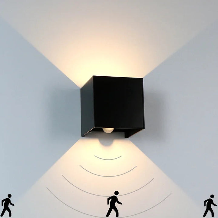 Modern cube outdoor LED wall light with motion sensor illuminating a garden