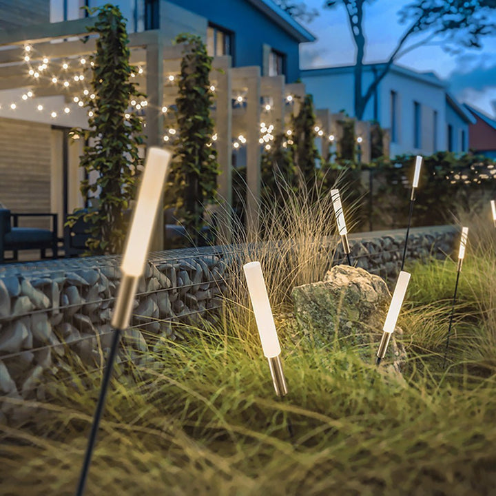 Modern cylindrical solar LED stake light lining a garden pathway at night