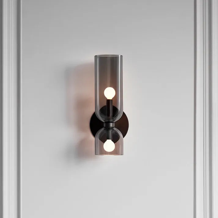 Glass cylinder wall sconce lit at night above bed