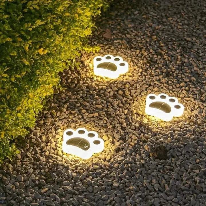 Solar LED paw-shaped garden light glowing warm white on a stone patio at dusk