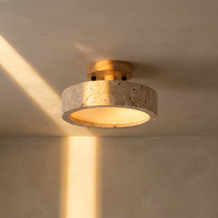 Aterna round travertine stone LED ceiling lamp on parchment plaster with warm amber glow, wabi-sabi editorial hero shot